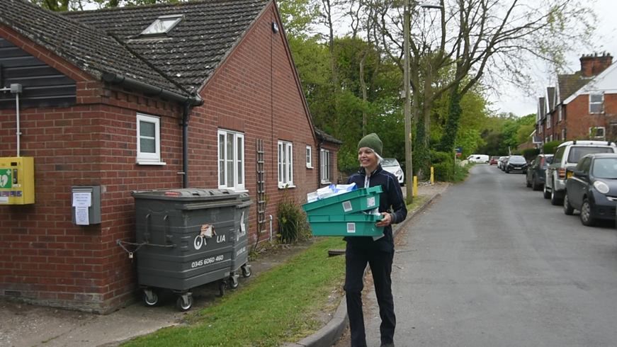 Council Officer delivering prescriptions, stood outside a surgery, holding two boxes of medicine.